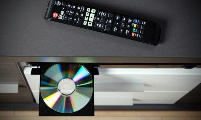 A top view of a DVD player with a disk inserted and a remote control resting directly above it.