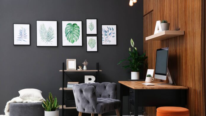 A home office with a dark gray color scheme and warm wood tones. A botanical theme is tied throughout the room with wall art.