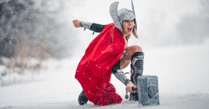 A woman in a costume resembling the Nordic god of thunder kneeling in snow and pretending to shout with rage.